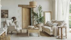 A white living room with seats, a wooden coffee table with decor on it, a woven rug, and a wooden door