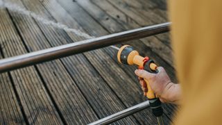 hand using hose to rinse wooden decking