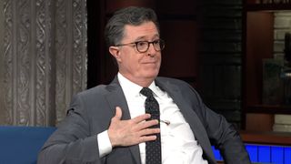 Stephen Colbert holding hand to chest while talking to Jon Baptiste on The Late Show