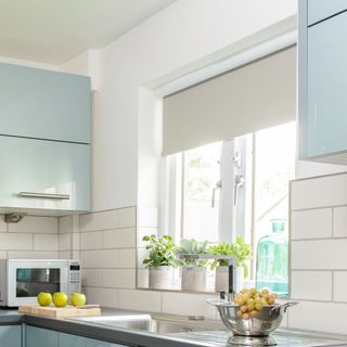 A kitchen with light blue glossy cabinets and white roller blinds in the window