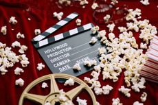 Clapperboard, film reel, film and spilled popcorn on red satin background