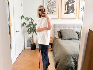 Natalie Cantell taking a mirror selfie in her NYC apartment wearing an oversize white Tibi t-shirt, denim Tibi skirt, Celine eyewear, and brown Havaianas flip-flops.