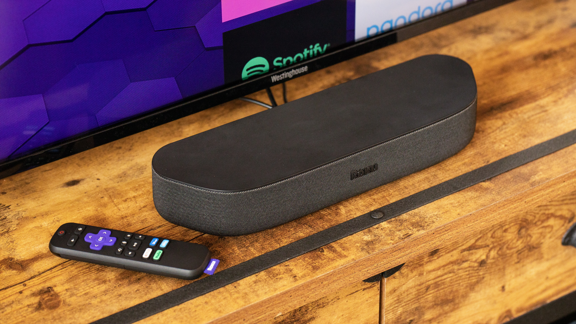 Roku Streambar on a counter in front of a TV next to a Roku remote
