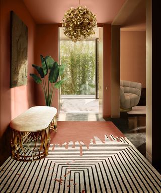 Summer entryway decor in blush pink and gold tones, with Valencia striped rug, Mecca bench, McQueen gold chandelier