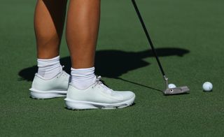 A close up of Tom Kim's Nike shoes and putter
