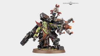 An Ork model stands on a plain background, weapon raised