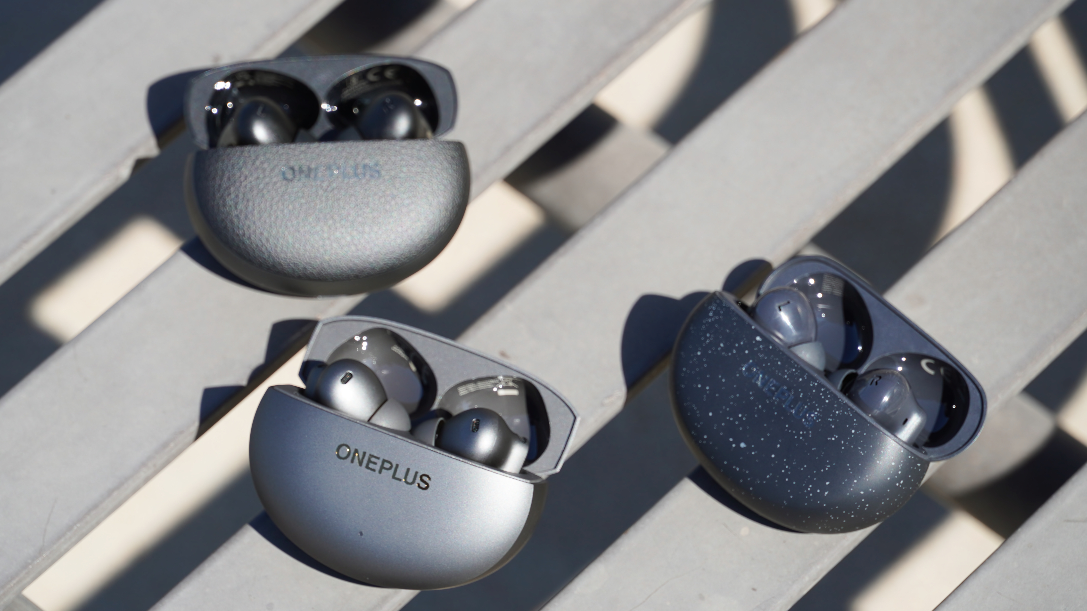 The OnePlus Buds 4 in Storm Gray beside the OnePlus Buds 3 Pro and OnePlus Nord Buds Pro 3.