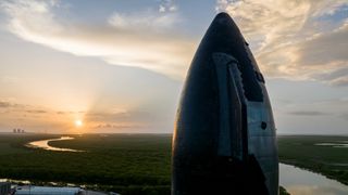 closeup of a conical rocket nose towering above a wetland landscape at sunset