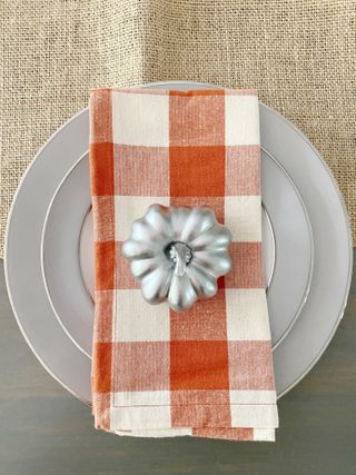 Silver painted glass pumpkin on checked orange napkin on a gray plate
