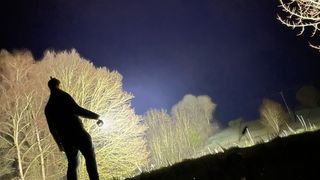 The Acebeam X75 being shone into distant trees by a person with their back to the camera