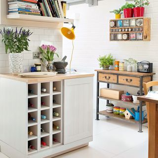 A white kitchen with eclectic shelving, a yellow lamp and a wine rack