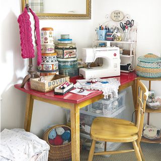 room with white wall and sewing machine on wooden table and mix colour wool ball in wooden basket under table