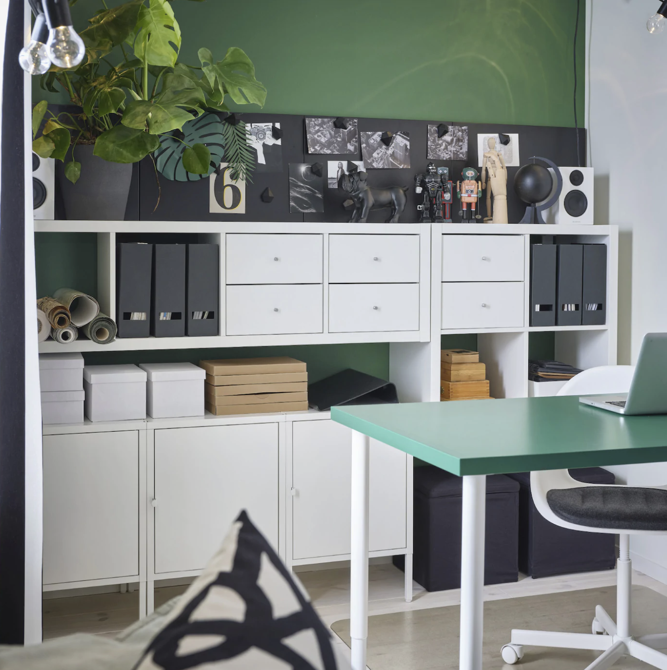 built in white storage unit full of folders and boxes, in front of a green wall and next to a green desk with a white and black chair