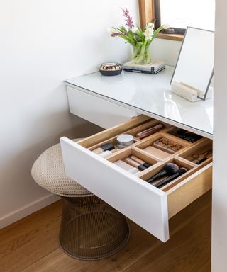 Organized drawer in a white vanity with flowers and a mirror on the countertop