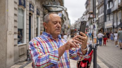 A retiree looks at his phone while standing in the historic center of the city of Porto, Portugal.