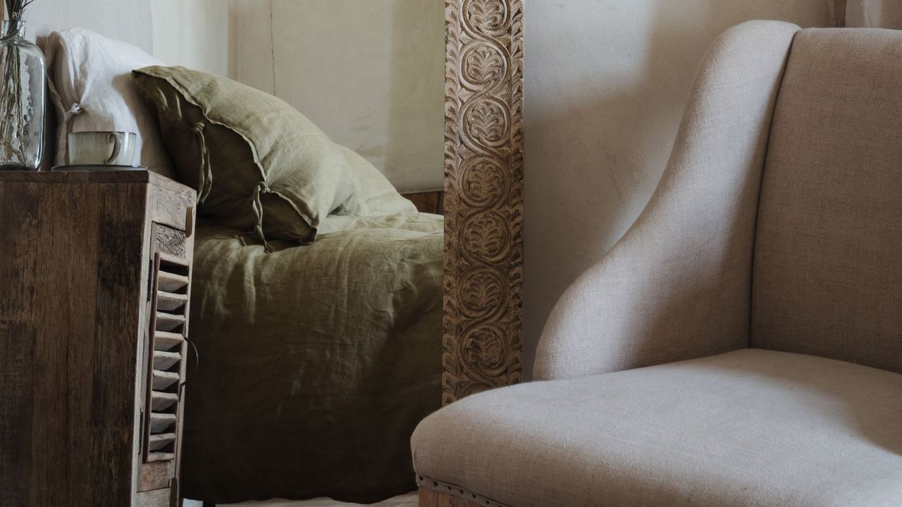 A cream bedroom chair next to a large mirror, reflecting a green linen bed