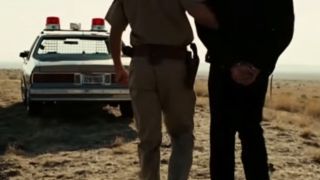 A police officer escorting a handcuffed man to police car in No Country For Old Men