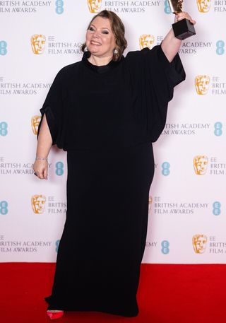 Joanna Scanlan poses on the red carpet holding a bafta in a black dress with voluminous sleeves