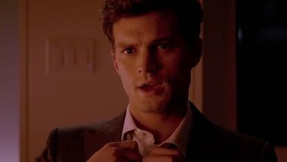 Jamie Dornan untying his shirt button in a scene from 'Fifty Shades of Grey'
