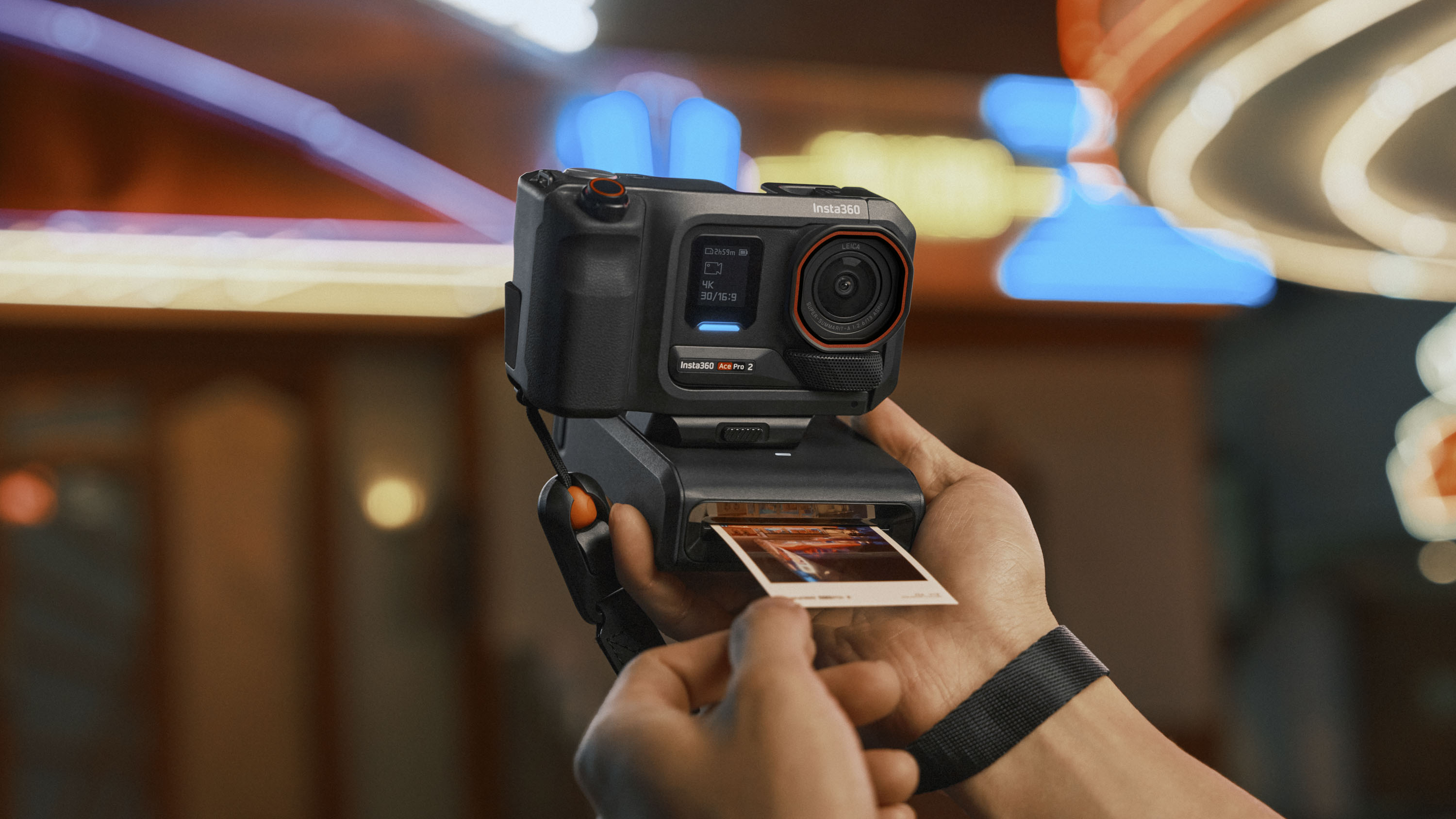 Insta360 Ace Pro 2 action camera housed inside grip accessory and clip-on instant printer, with bright neon night lights in background