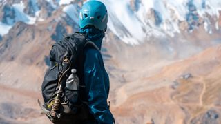 A mountaineer carrying an ice axe on their pack looks at the snow covered mountains