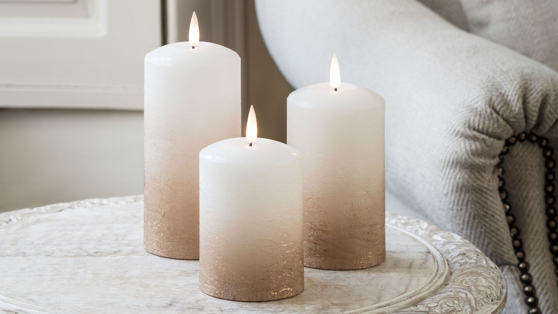 Best flameless candles with gold ombre on aside table next to a linen armchair