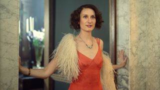 Bessie Carter in a red dress and white feather boa as Nancy Mitford in Outrageous