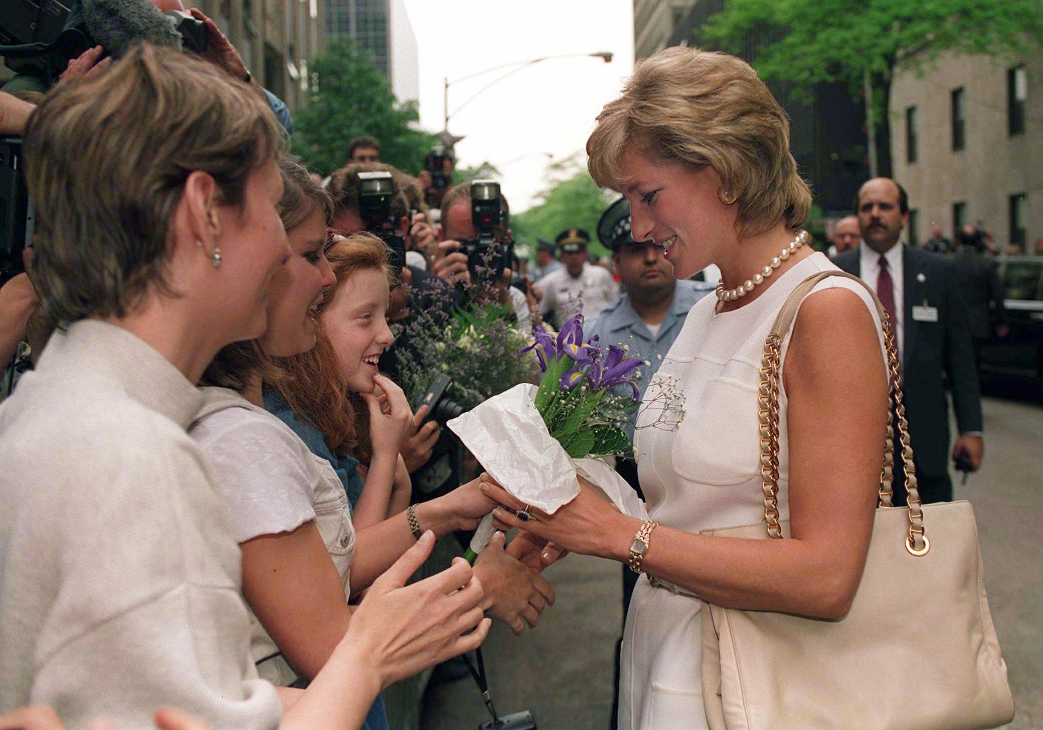 Princess Diana wearing a sleeveless ivory dress and pearls talking to fans in Chicago in 1996