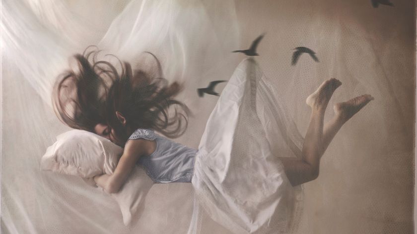 A dream-like image of a woman asleep in bed, with her hair and bedding flying about her as if she is floating in the air.