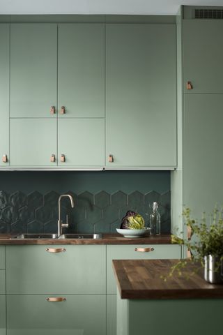 Hexagonal green tiles as a backsplash with matching painted wall in a green kitchen