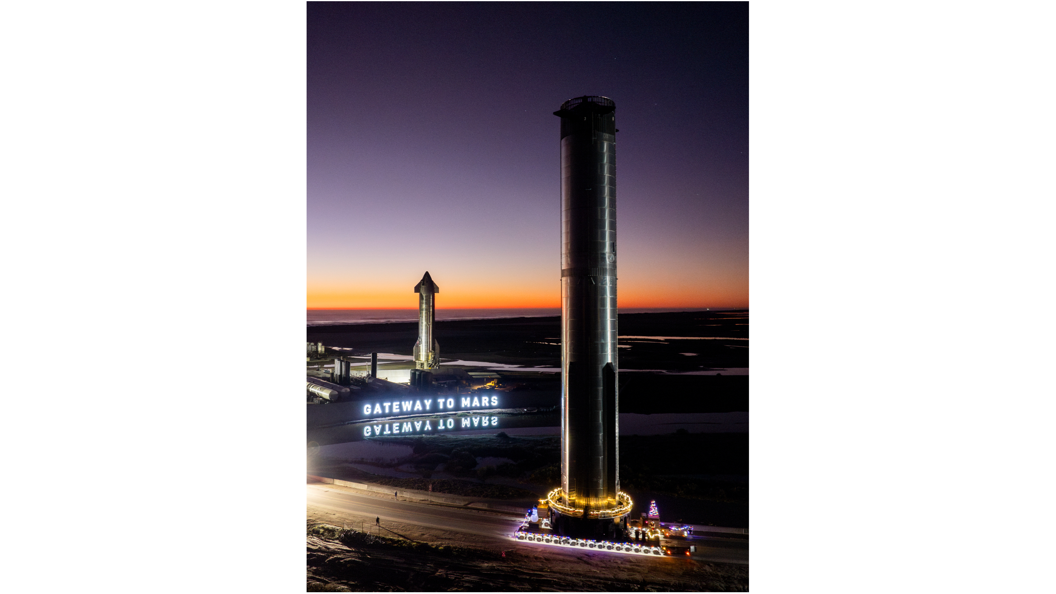The rocket's booster and upper stage are positioned vertically against a dark sky, near a white illuminated sign that says 