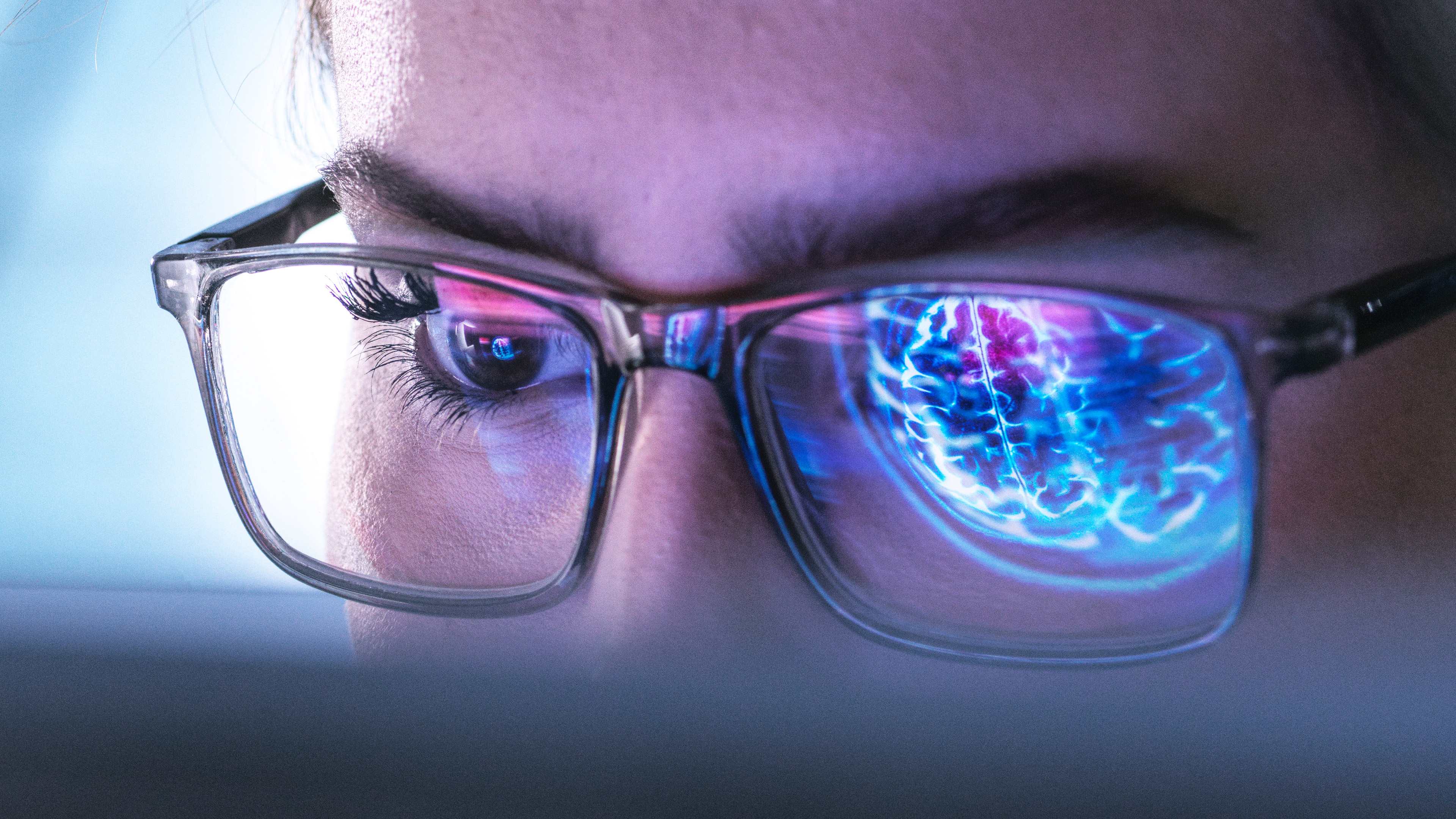 A close up of a person's eyes and face. They are wearing glasses and in one eye there's. a reflection of a digital brain