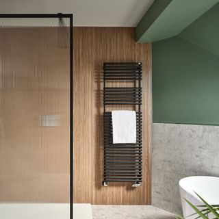 a bathroom with a bathtub, a reeded shower screen, green walls, and a black towel rail