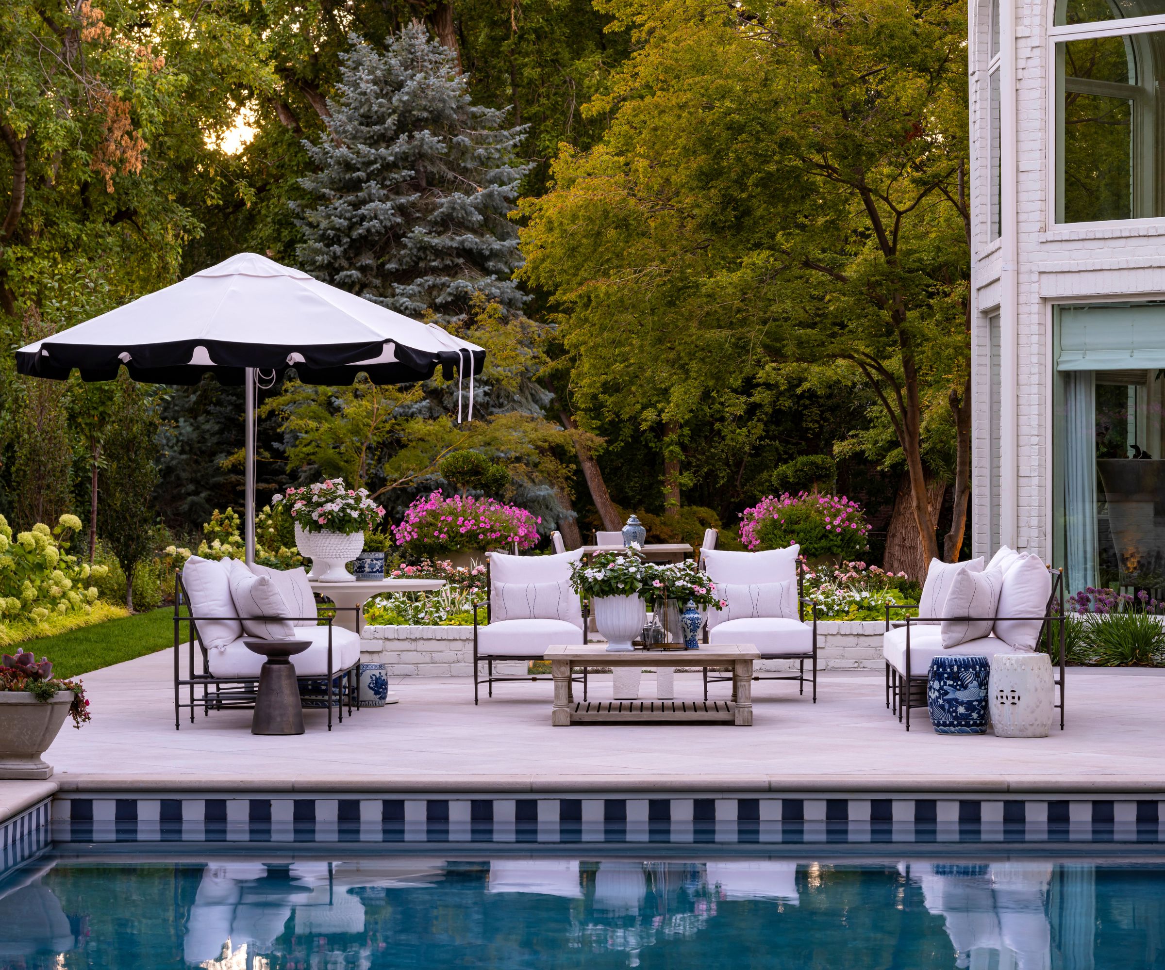 Outdoor seating area by a pool with large pots of flowers and a white parasol