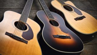 Three acoustic guitars lie on a wooden floor