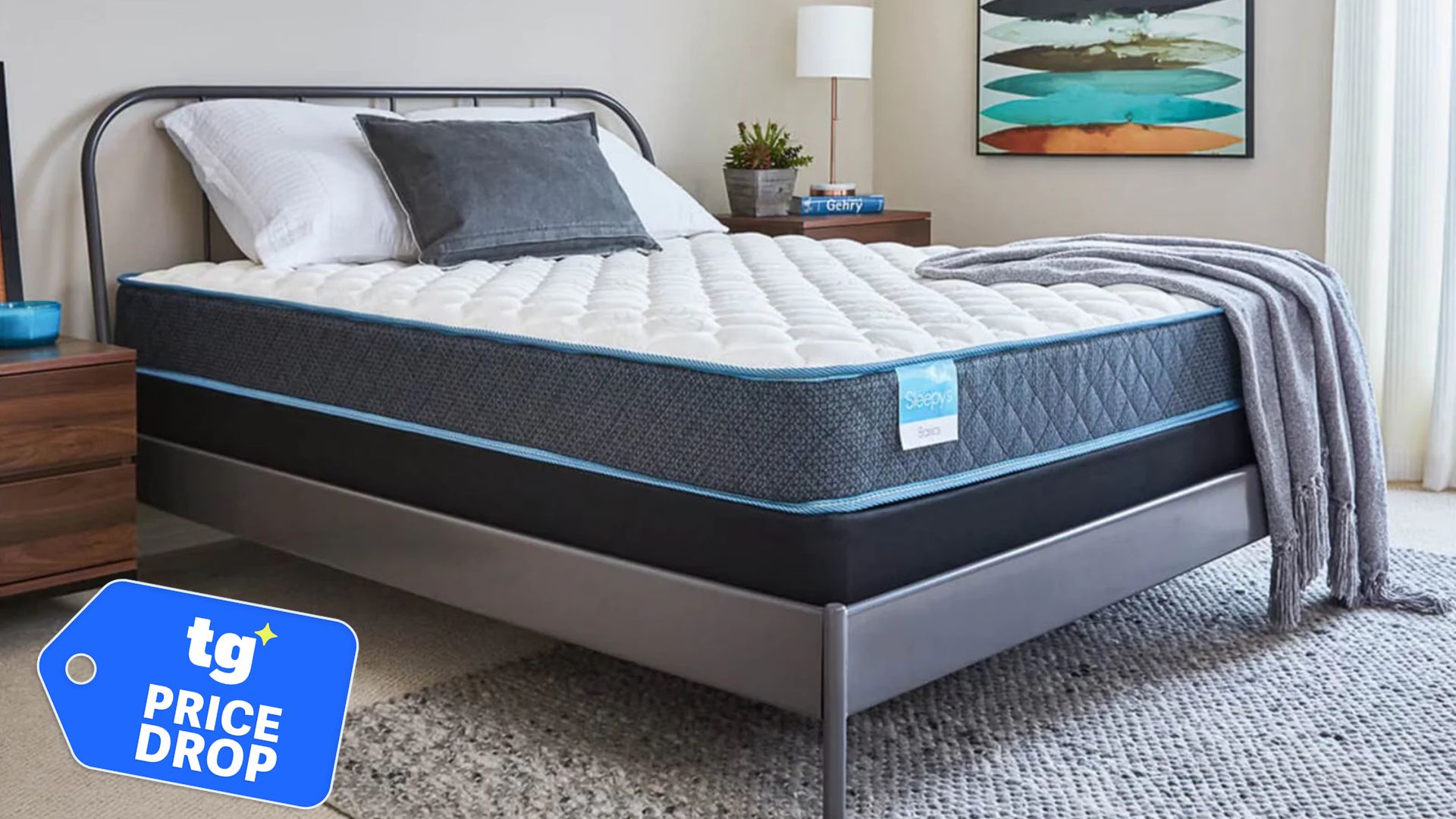 The Sleepy's Basic Innerspring Firm Mattress in a bedroom. In the bottom left hand foreground. there is a "Price Drop" deals badge.