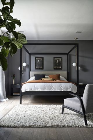 Bedroom with four poster bed, armchair, gray walls, gray wood floor and rug