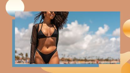 Young woman with curly dark afro hair walking along the beach wearing a black bikini