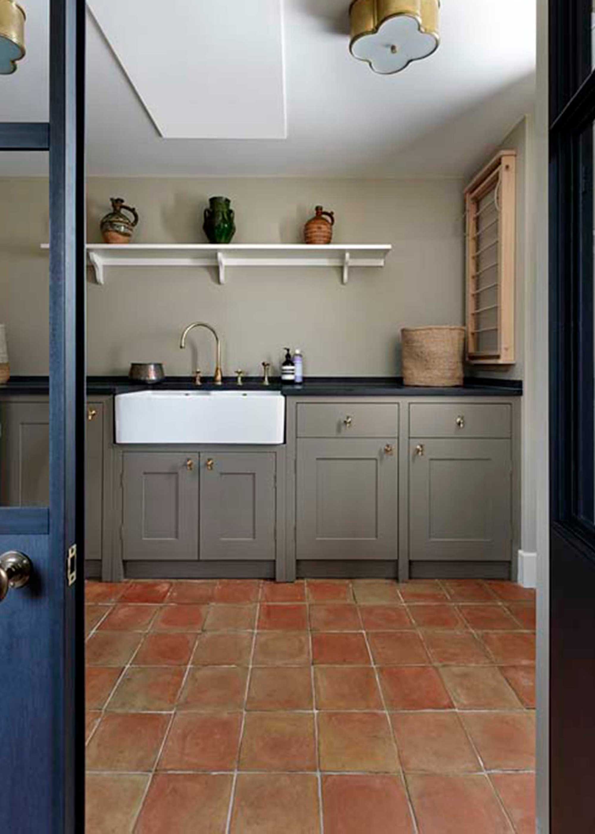 Laundry room with quarry tile flooring. There are also greenish/grey cabinets in the kitchen with open shelving.