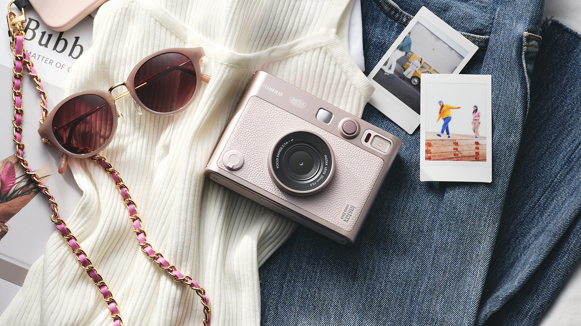 Fujifilm Instax Mini Evo Gentle Rose instant camera on a pile of clothes next to INstax Mini prints