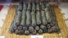 Photograph of stacks of bundled Japanese coins atop a straw woven mat upon a white tabletop.