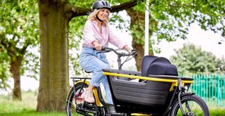 A women rides a black and yellow Raleigh Stride cargo bike in a park