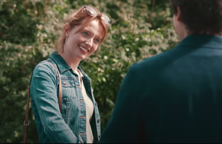Poppy Gilbert as Abbie Collier, smiling at someone and wearing a denim jacket