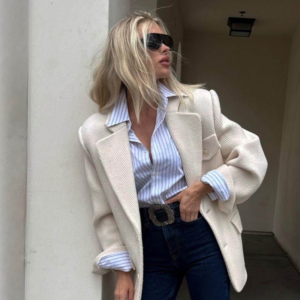 Elsa Hosk poses wearing dark wash cropped jeans with black loafers. She tucked a striped shirt into her jeans and layered a cream blazer on top.