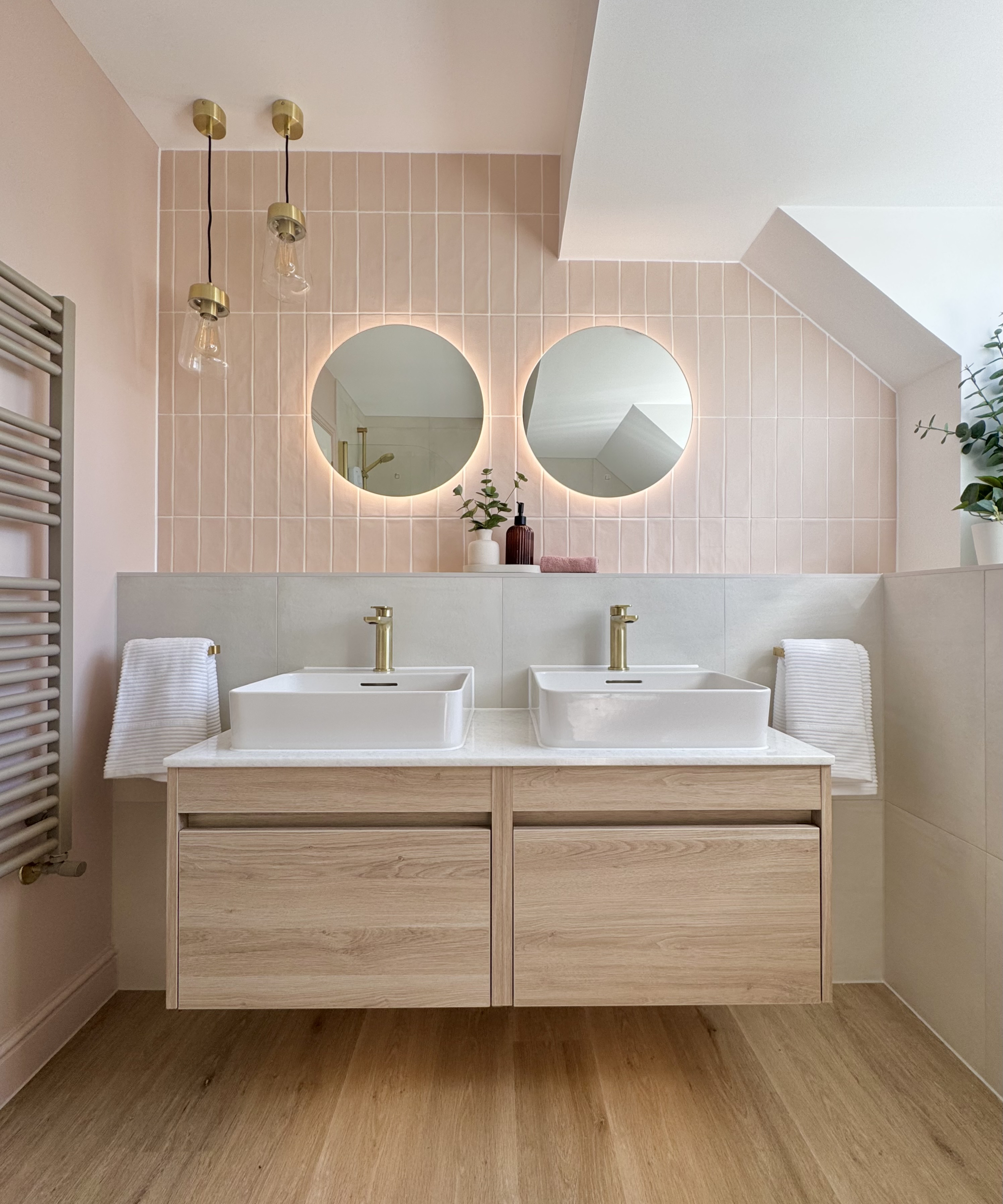 bathroom with wooden floor, wooden double vanity with white worktop, white ceiling, pink tiled walls, two mirrors above sink