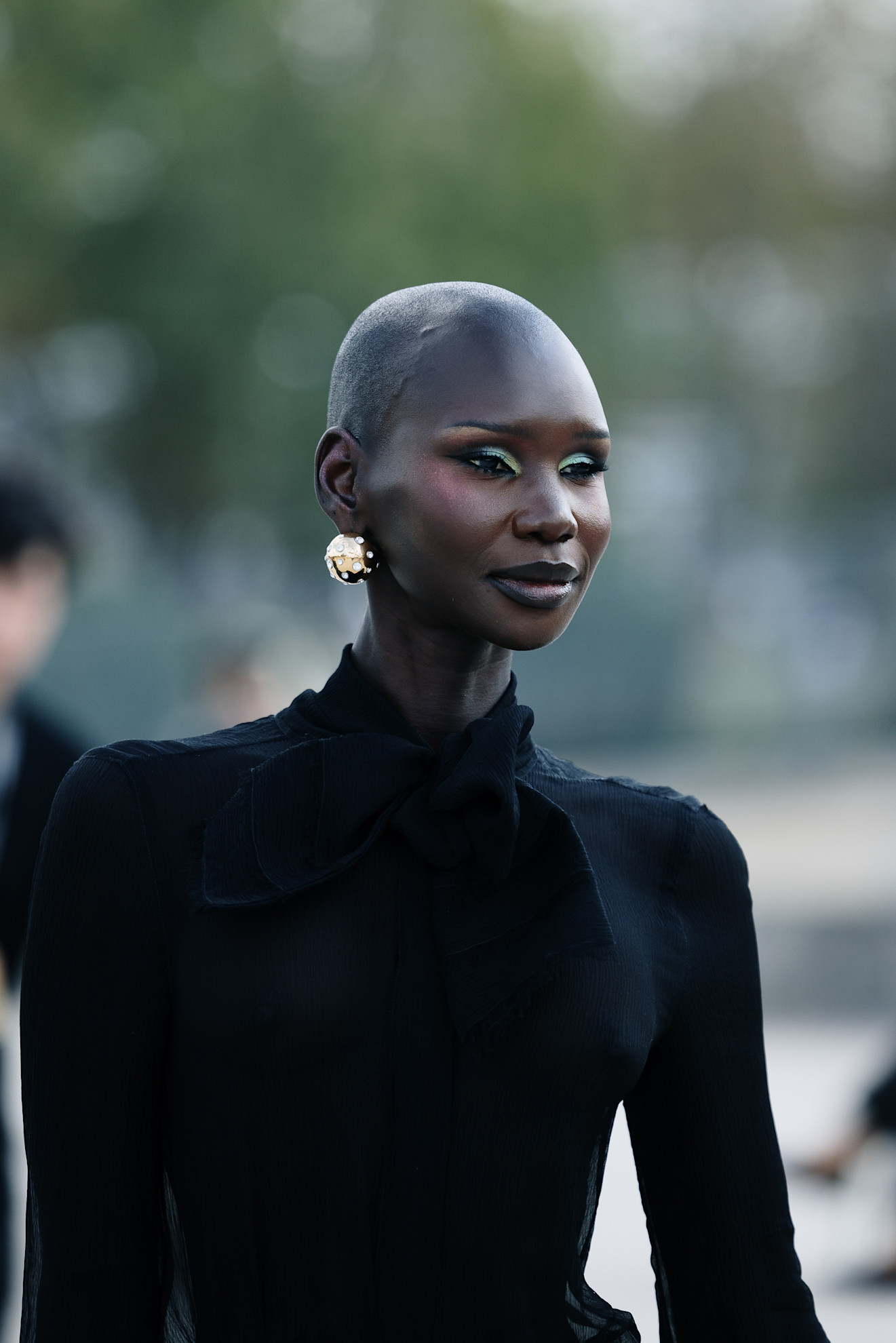 a black woman in a black dress with green eyeliner and silver earrings