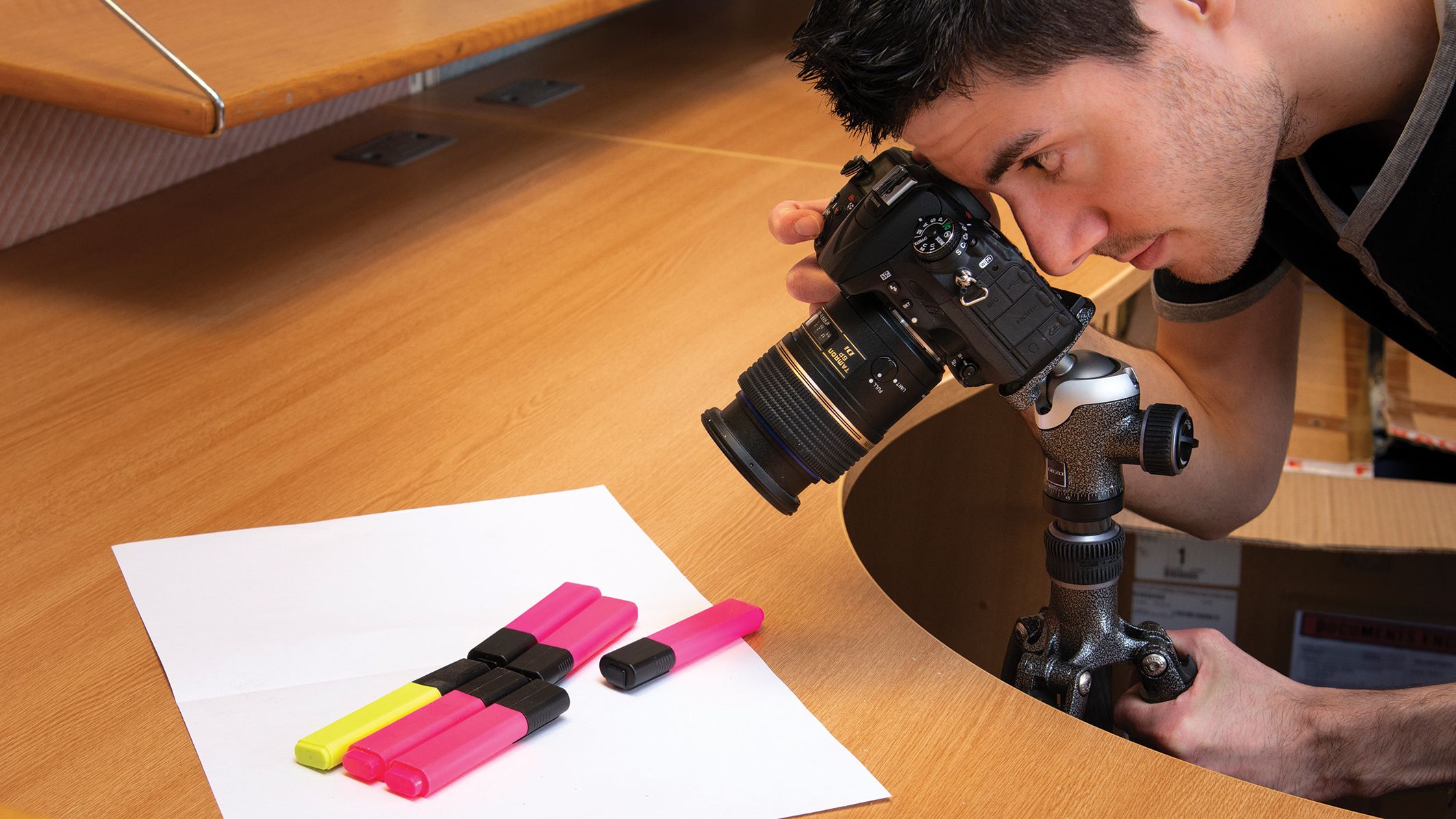 A person focuses a camera on a white sheet of paper with colorful highlighters arranged neatly on a wooden surface