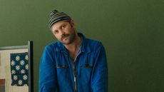 Alex Tieghi-Walker, a man in a blue jacket, stands against green wall