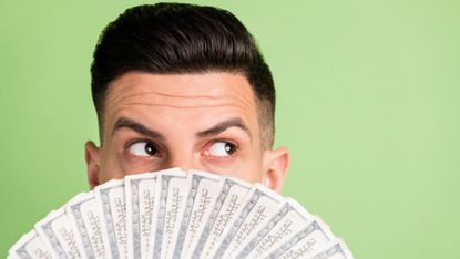 A man hiding his face with a fan of US currency