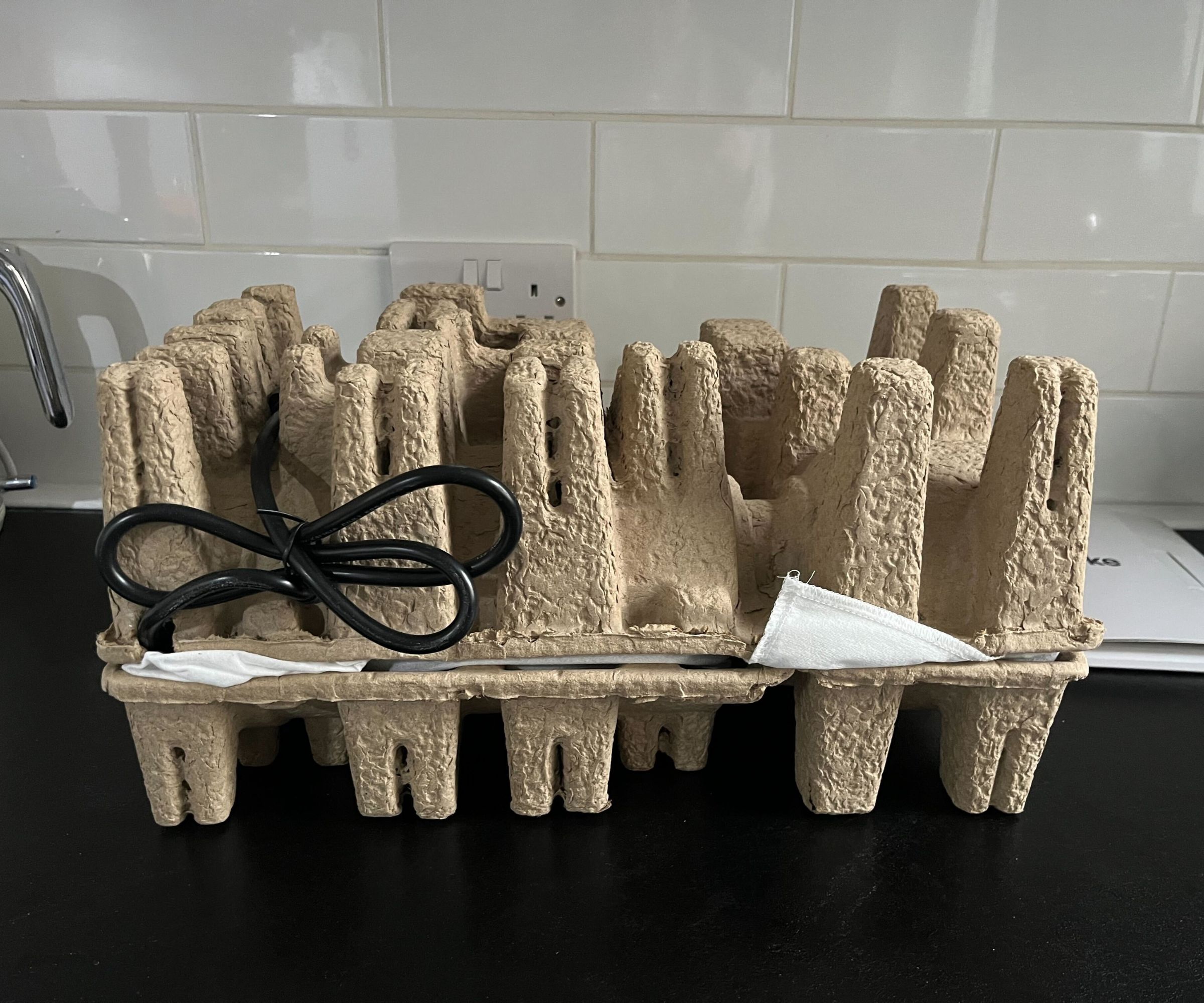 Cardboard egg-carton-esque packaging on a lack counter wit white subway tiles behind. 